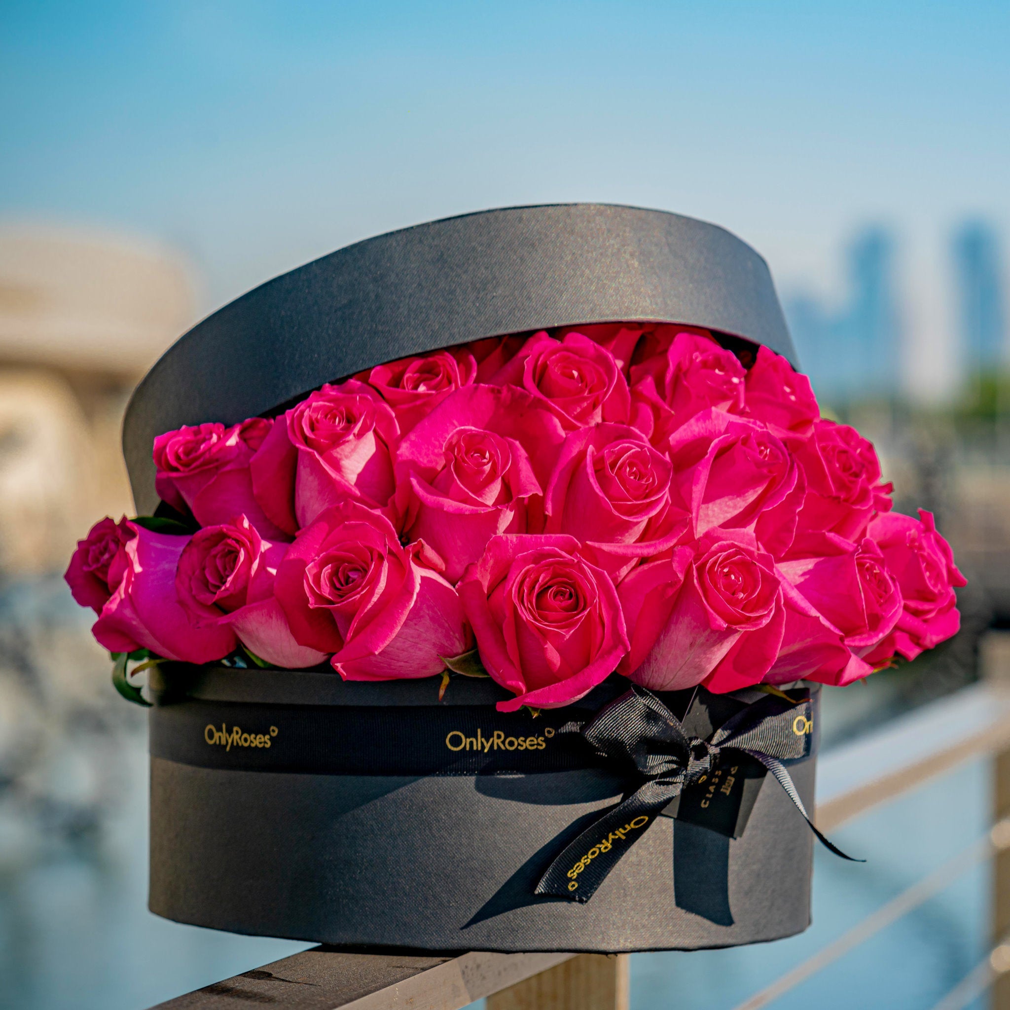 Gray box with pink roses and a black bow against a blurred cityscape background