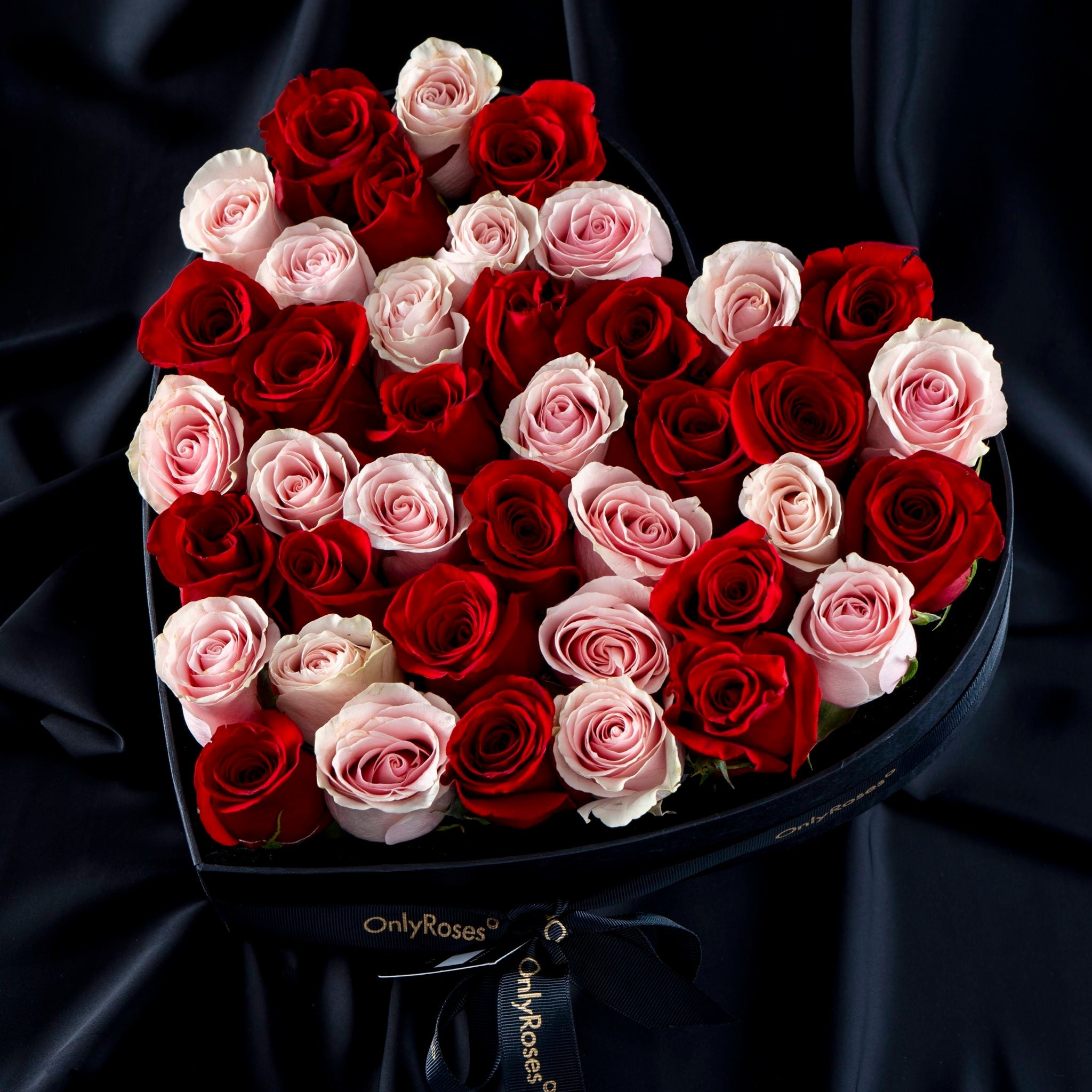 Heart-shaped bouquet of red and pink roses in a box with 'OnlyRoses' branding on a dark background.