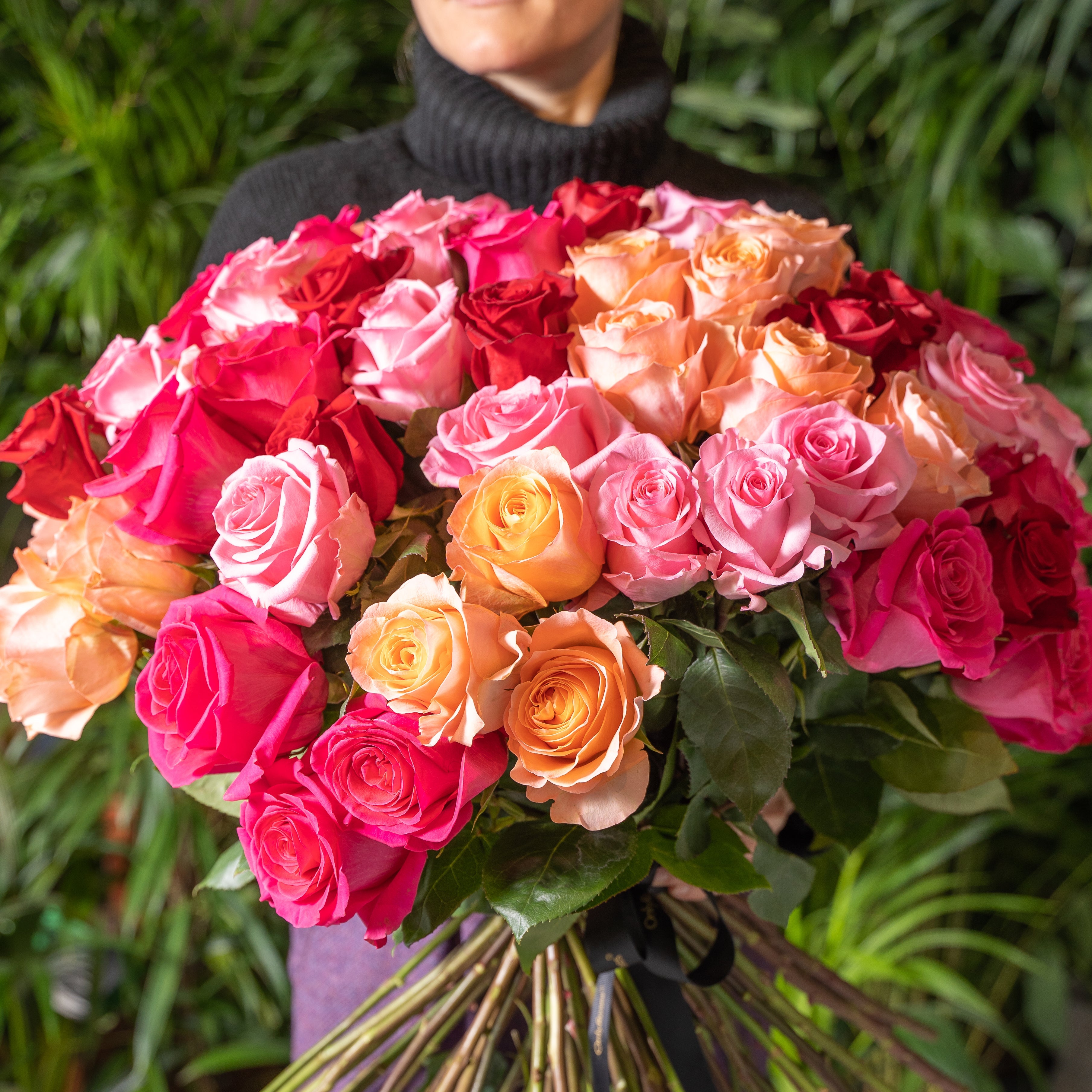 Bouquet of pink, red, and orange roses held by a person against a green background