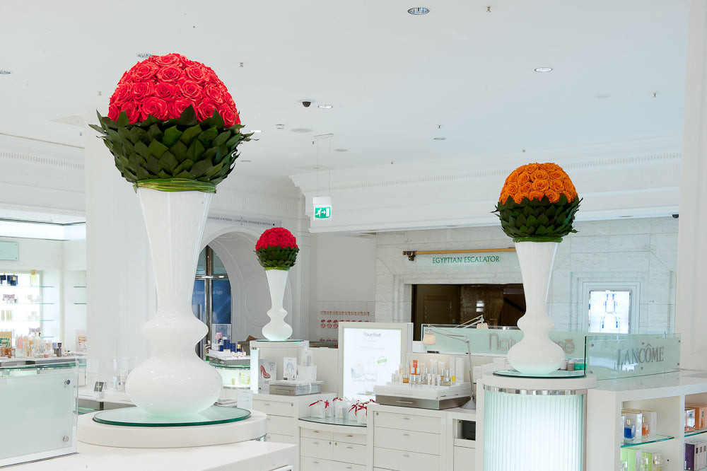 Decorative flower arrangements in tall white vases inside a modern building.