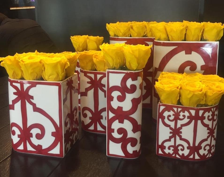 Yellow roses in red and white patterned containers on a dark surface