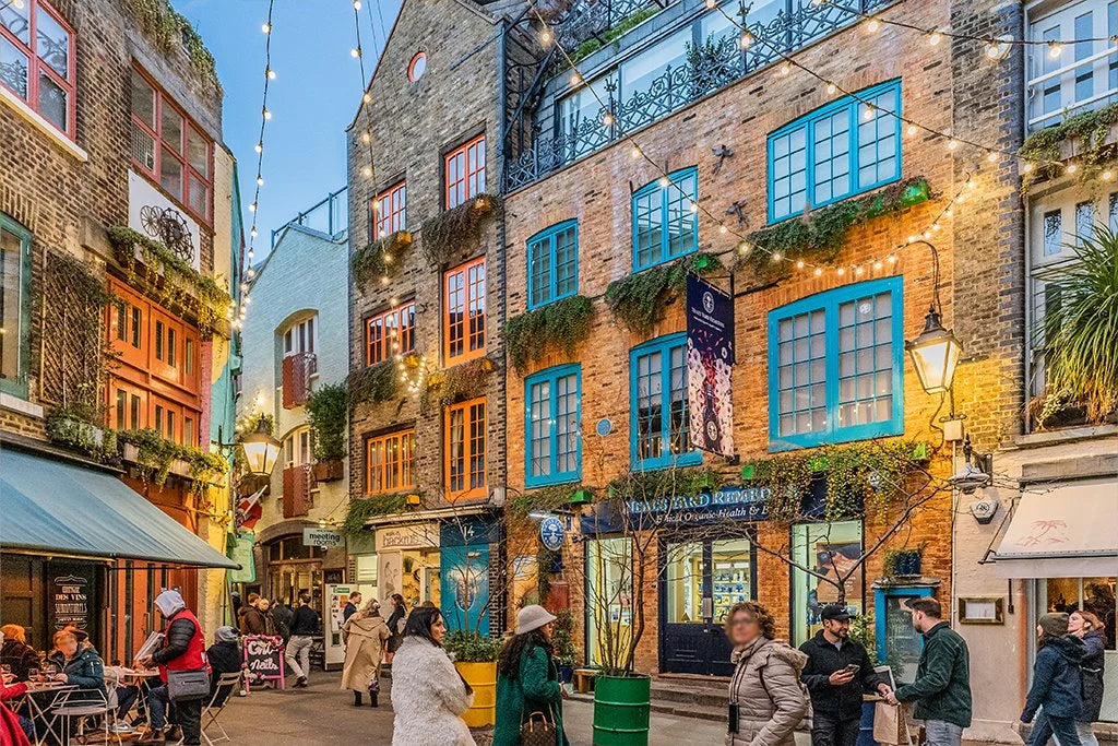 Street scene in a charming town with brick buildings, people walking, and string lights.