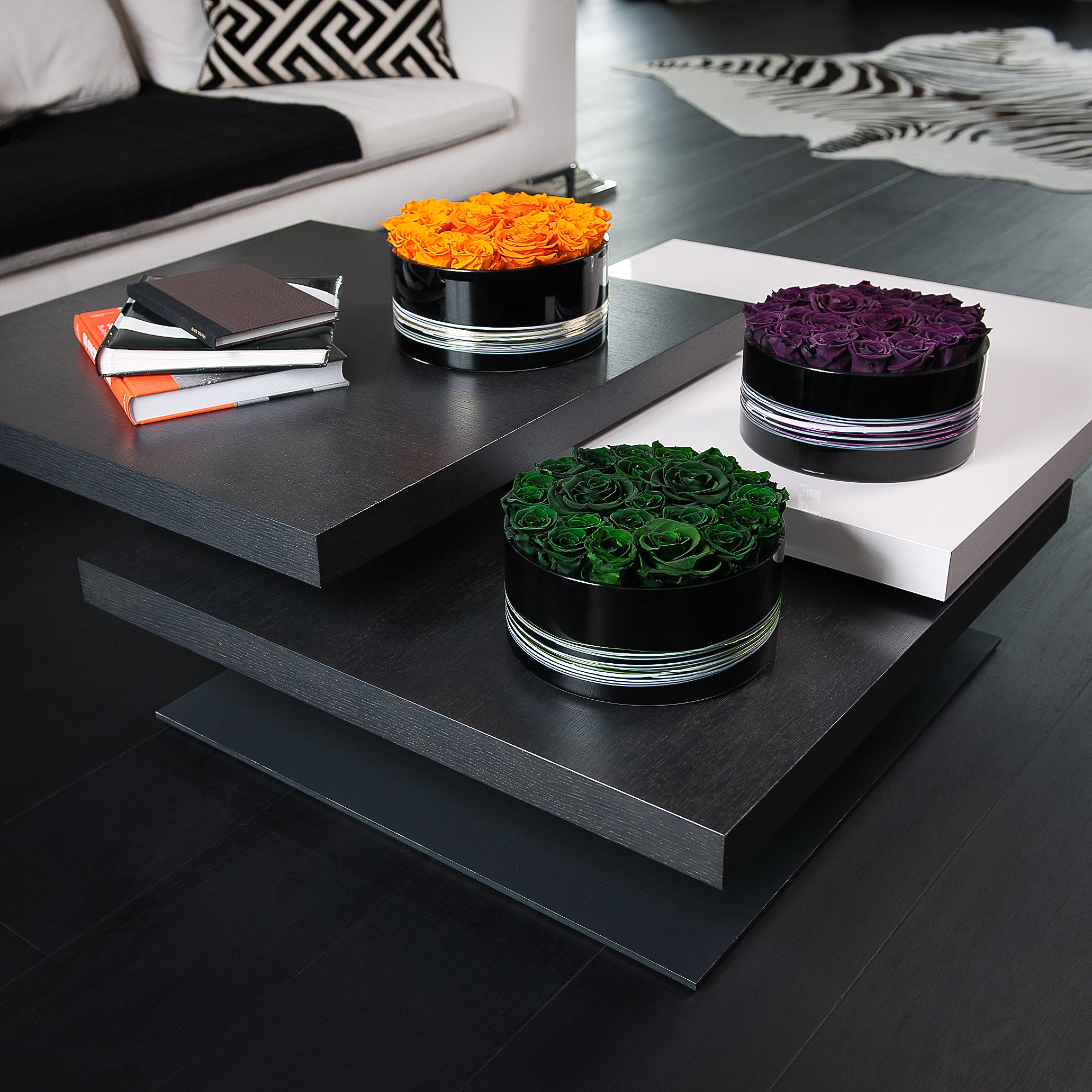 Three cylindrical containers with colored roses on a modern black coffee table.