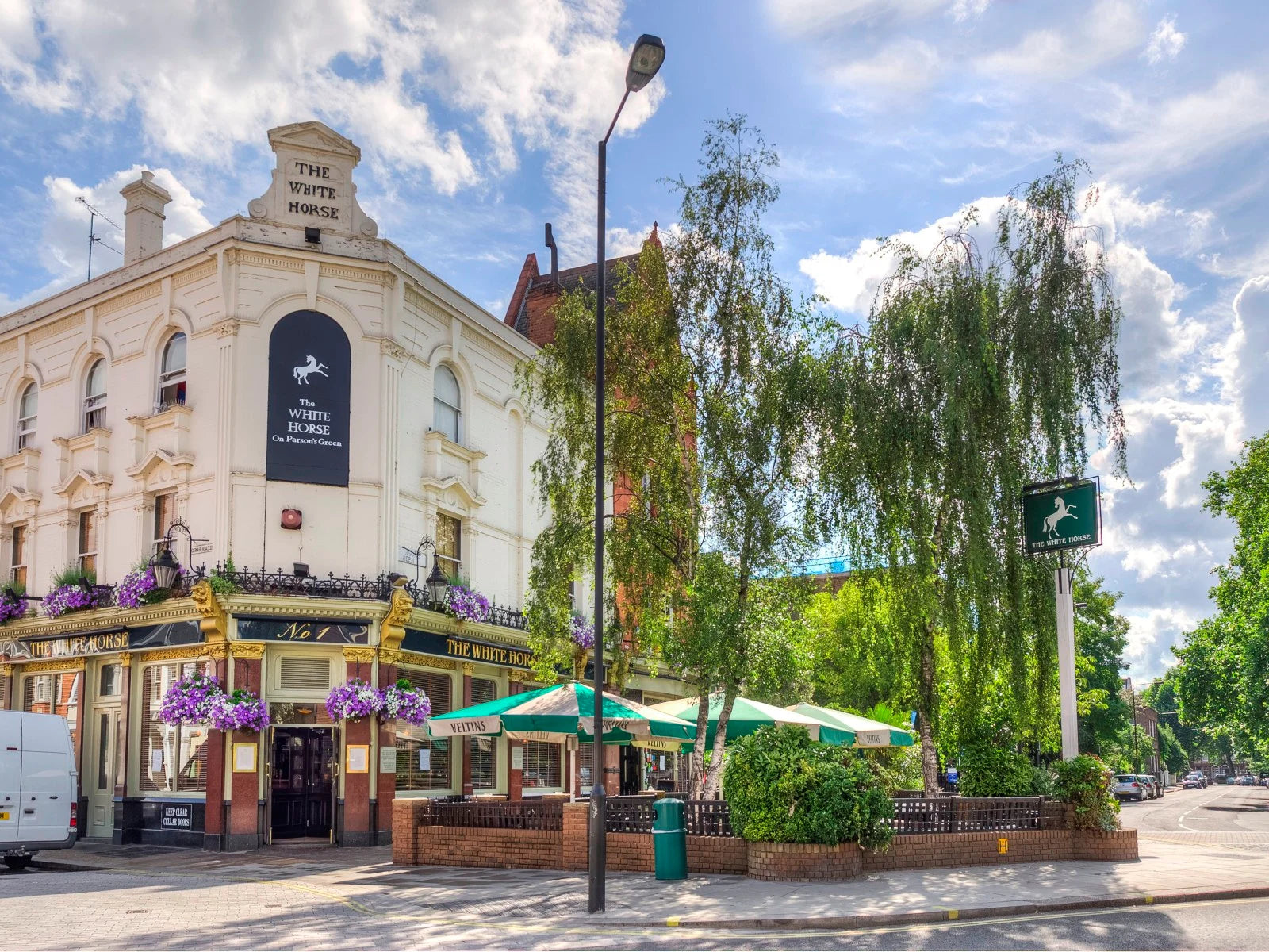 Pub named 'The White Horse' with green umbrellas on a sunny day.