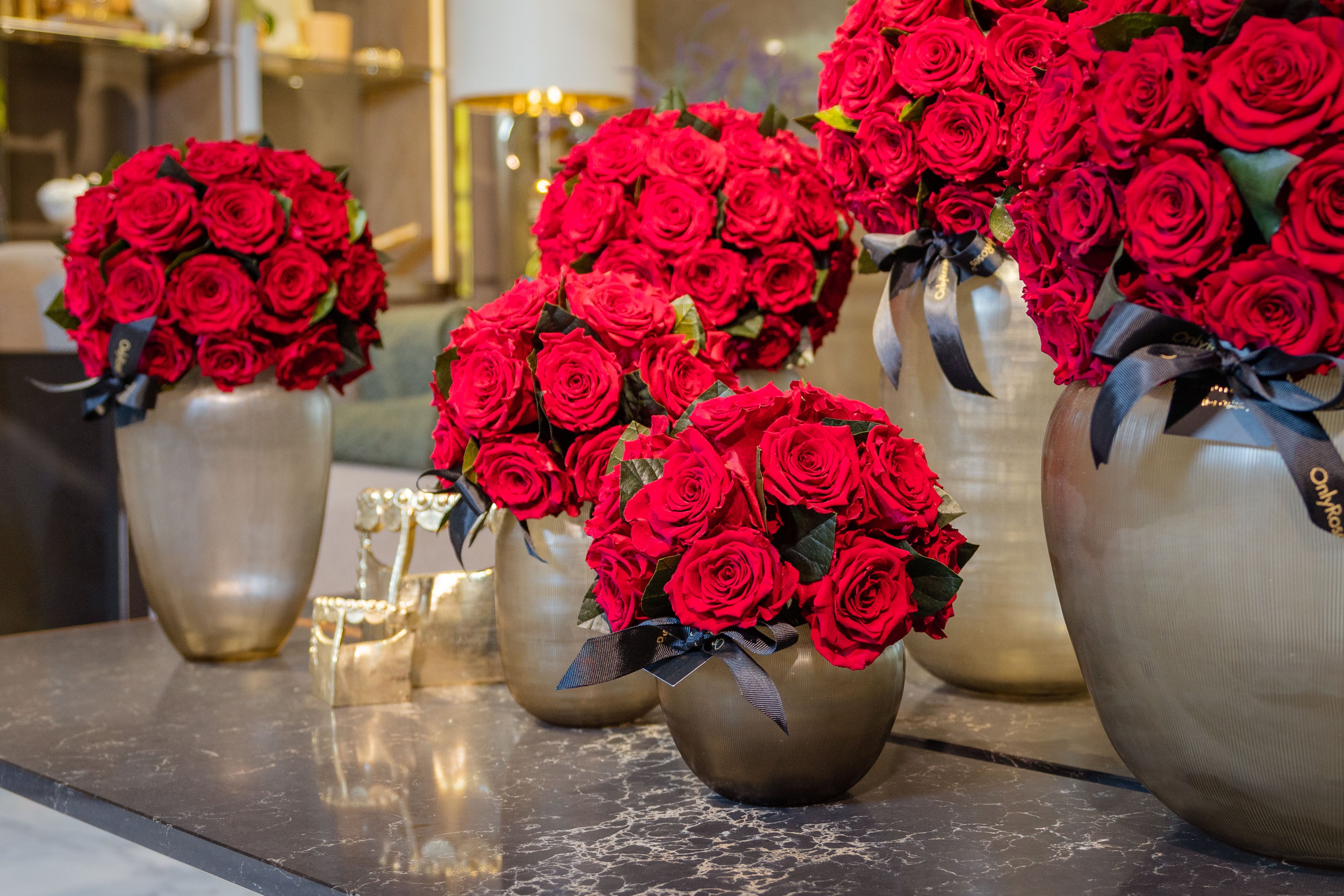 Decorative arrangement of red roses in silver vases on a marble surface.