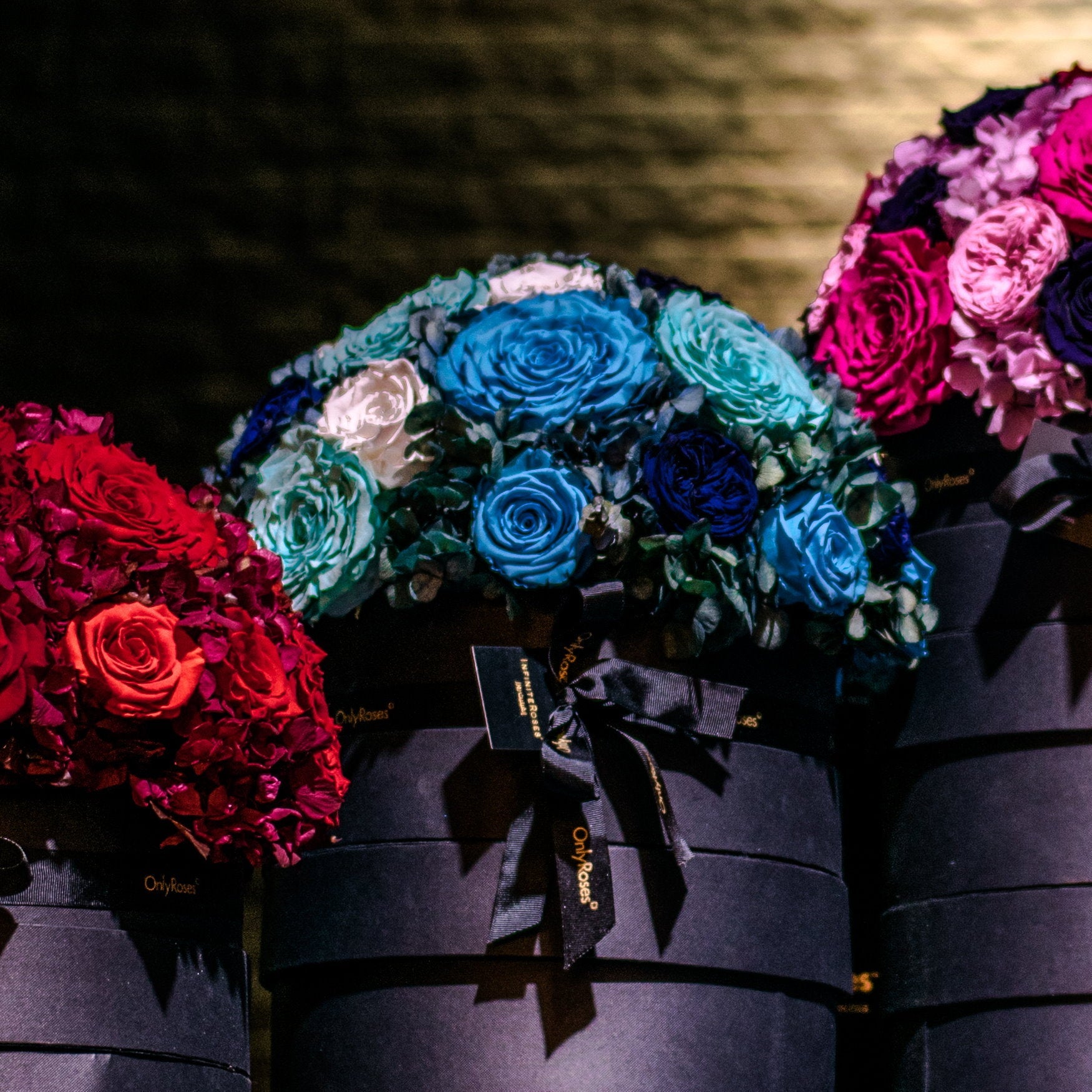 Three bouquets of roses in red, blue, and pink on black boxes with ribbons.