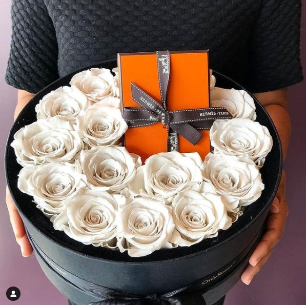 Round black box filled with white roses and an orange Hermes gift box.