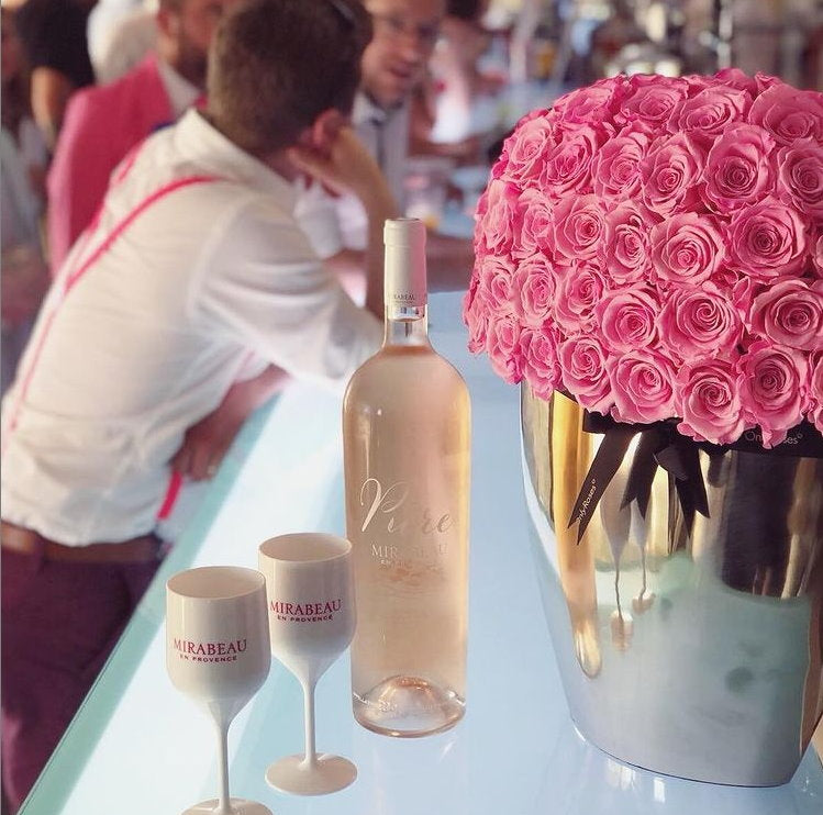 Bottle of wine and pink roses on a table with people in the background