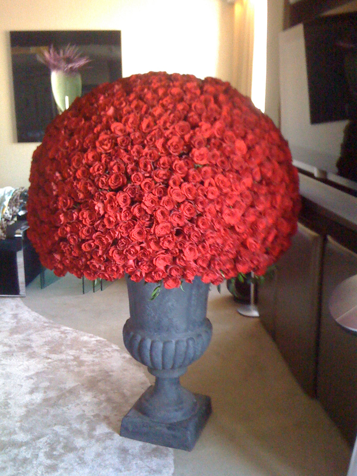 Large arrangement of red roses in a decorative urn on a table.