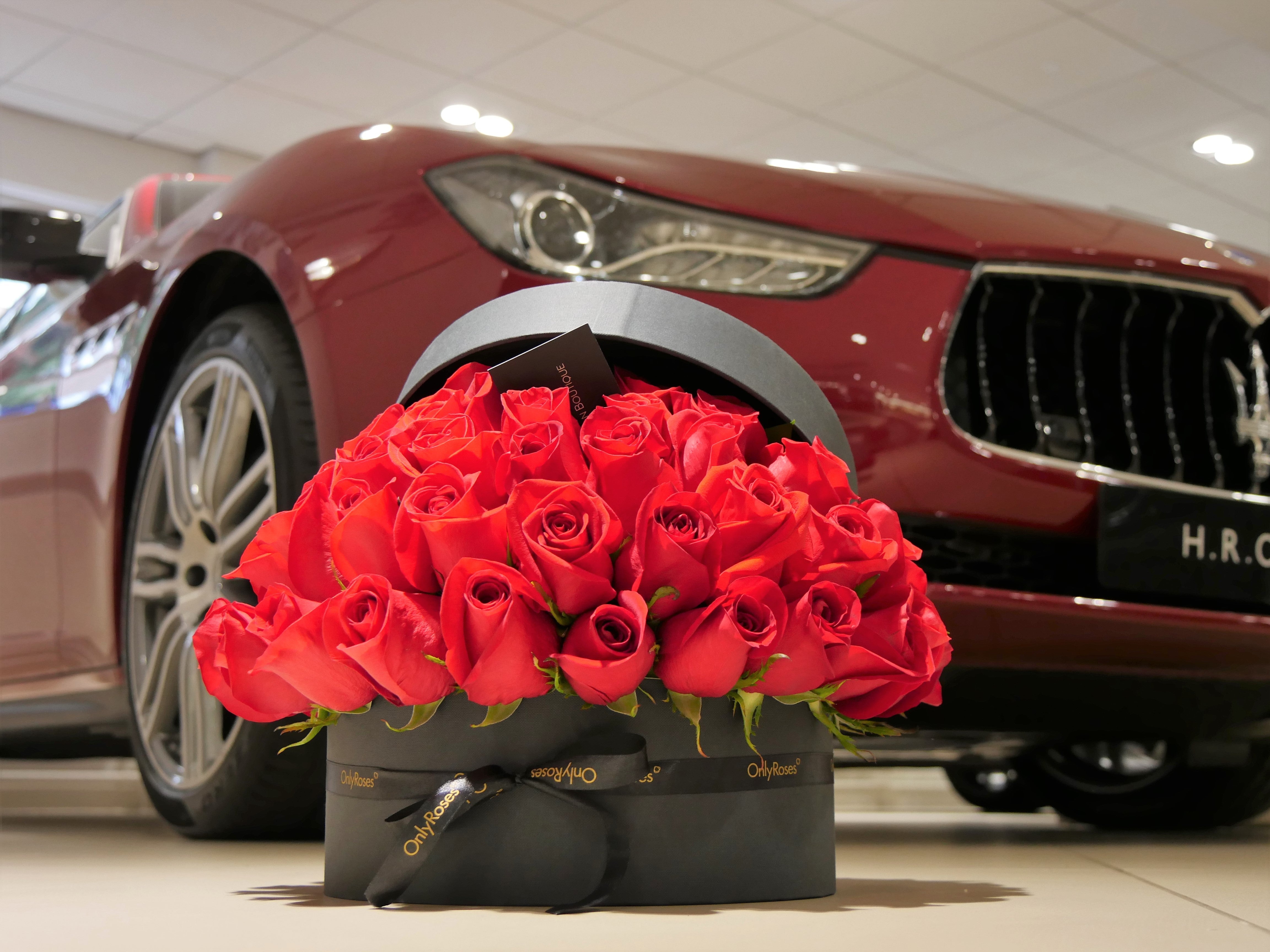 Bouquet of red roses in a black box in front of a red car