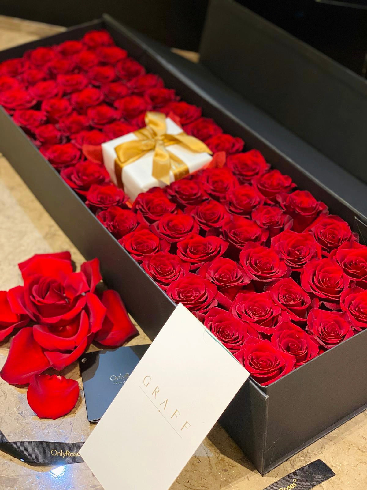 Box of red roses with a white box inside, on a light surface.