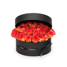 Black round box filled with red and orange roses on a white background