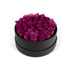 Black round box filled with purple roses on a white background