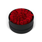Black round box filled with red roses on a white background