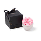 Pink rose in a white vase next to a black gift box with a bow on a white background