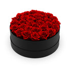 Black round box filled with red roses on a white background