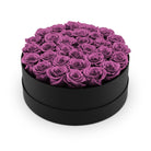 Black round box filled with purple roses on a white background