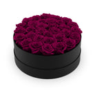 Black round box filled with purple roses on a white background