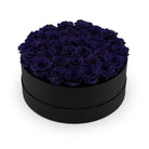 Black round box filled with purple roses on a white background