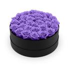 Black round box filled with purple roses on a white background