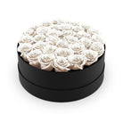 Black round box filled with white roses on a white background