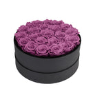 Black round box filled with purple preserved roses on a white background