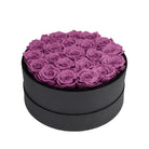 Black round box filled with purple preserved roses on a white background