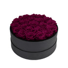 Black round box filled with purple roses on a white background