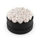 Black round box filled with white roses on a white background