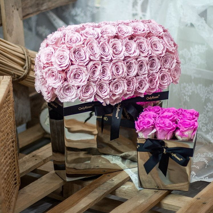 Two bouquets of pink roses in decorative boxes on a wooden surface.
