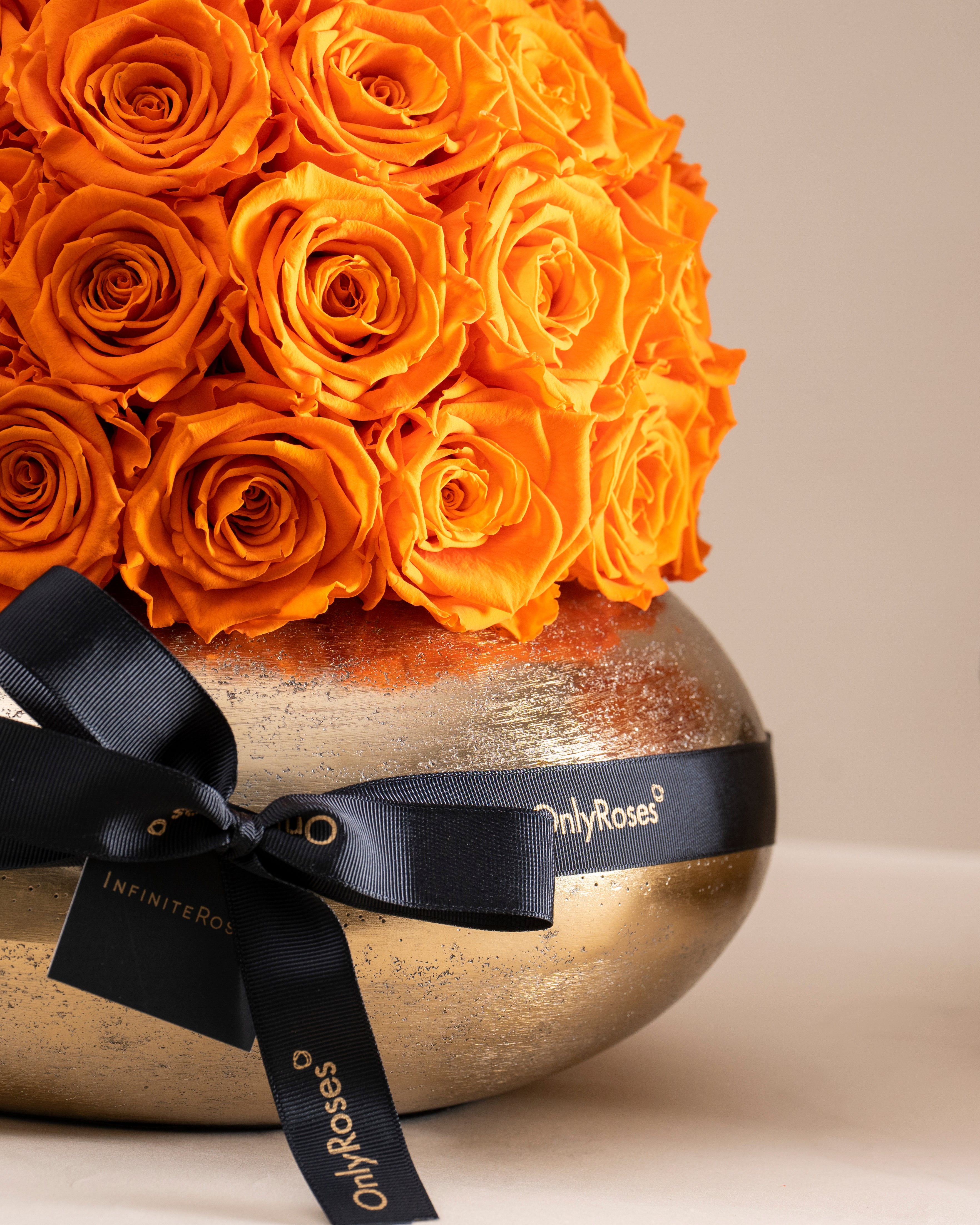 Bouquet of orange roses in a gold vase with a black ribbon, featuring 'Only Roses' branding.