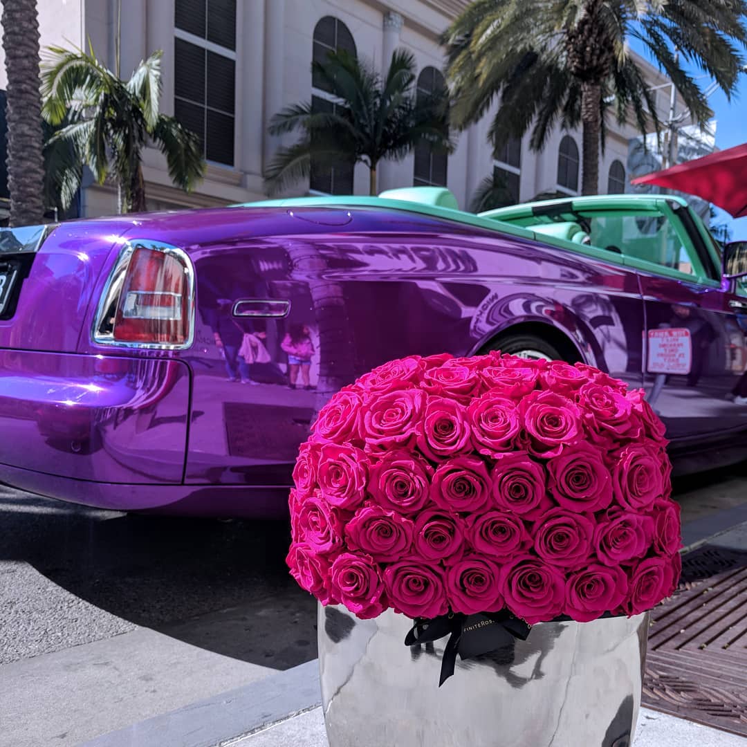 Purple Rolls-Royce car with a large bouquet of pink roses on a city street.