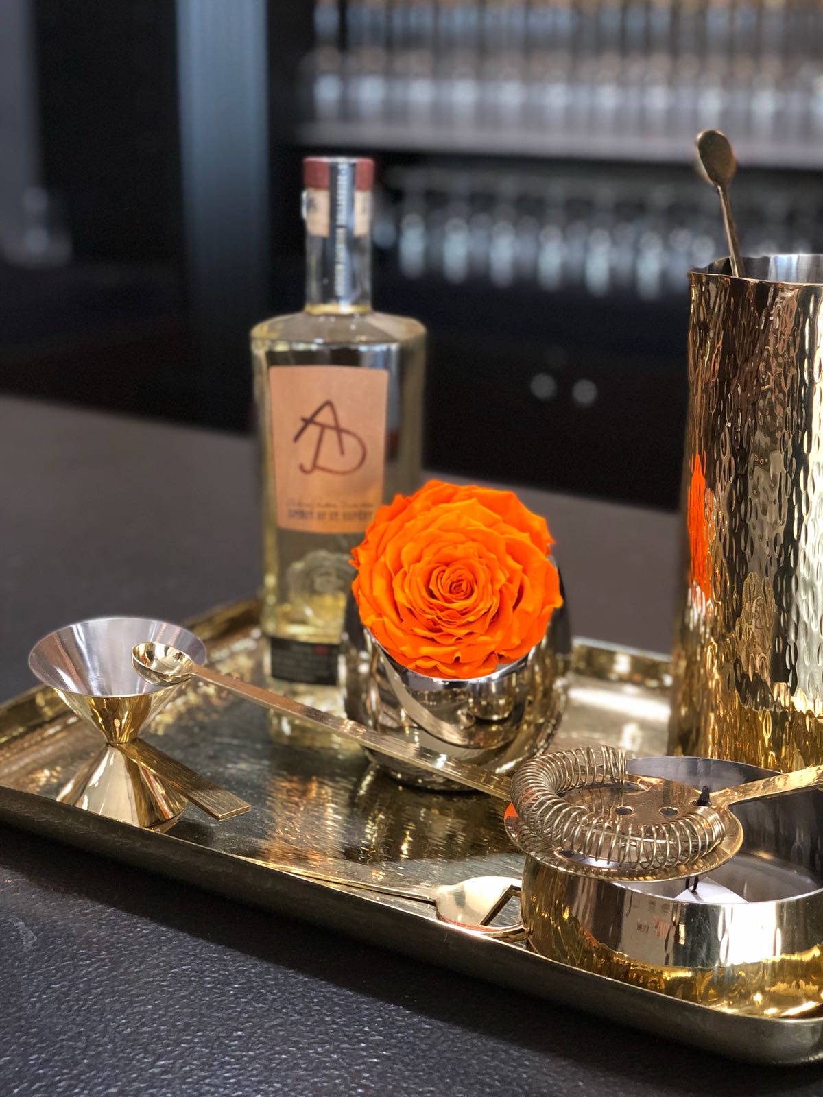 Bartending setup with a bottle, orange rose, and bar tools on a tray.