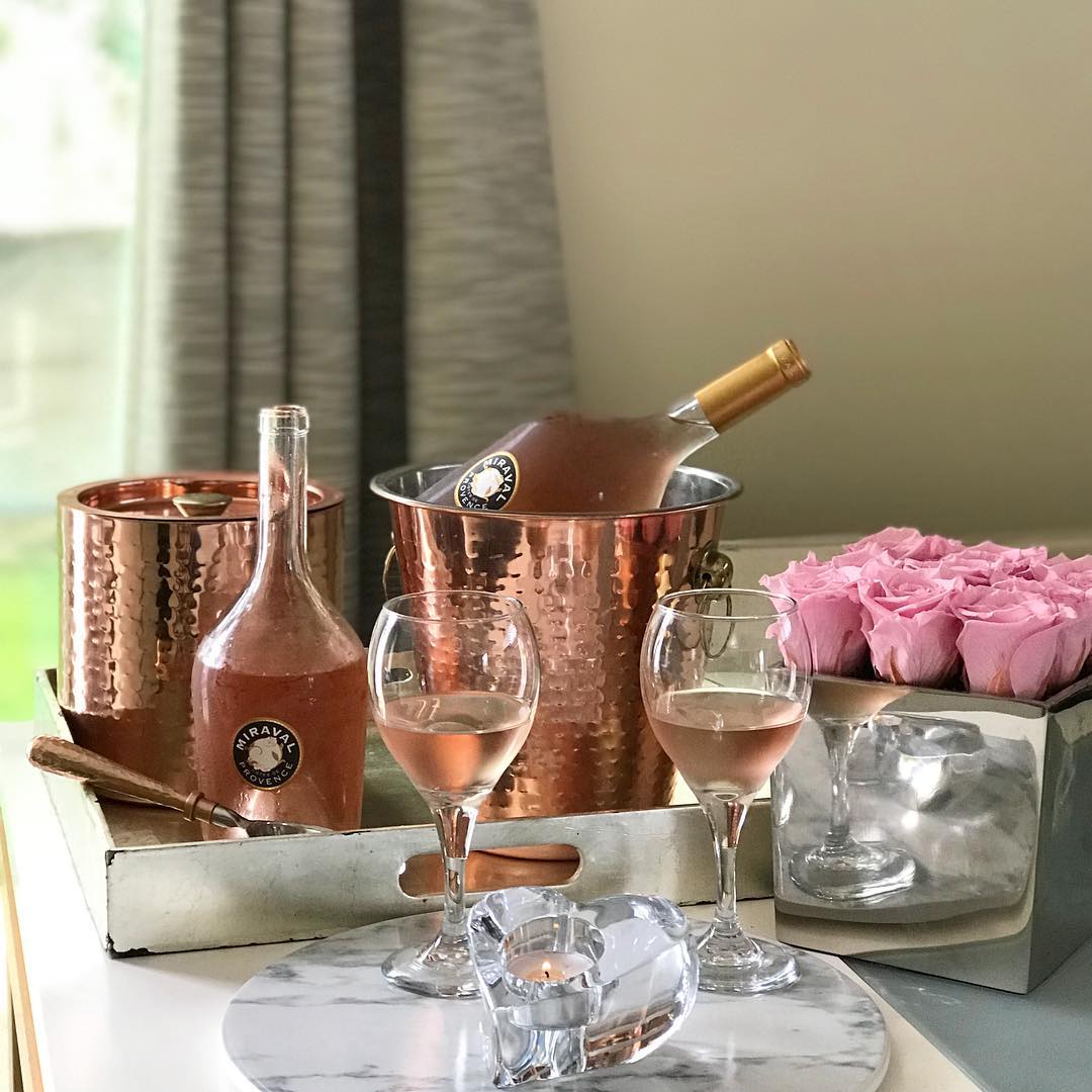Wine bottle, glasses, and pink roses on a tray with a neutral background