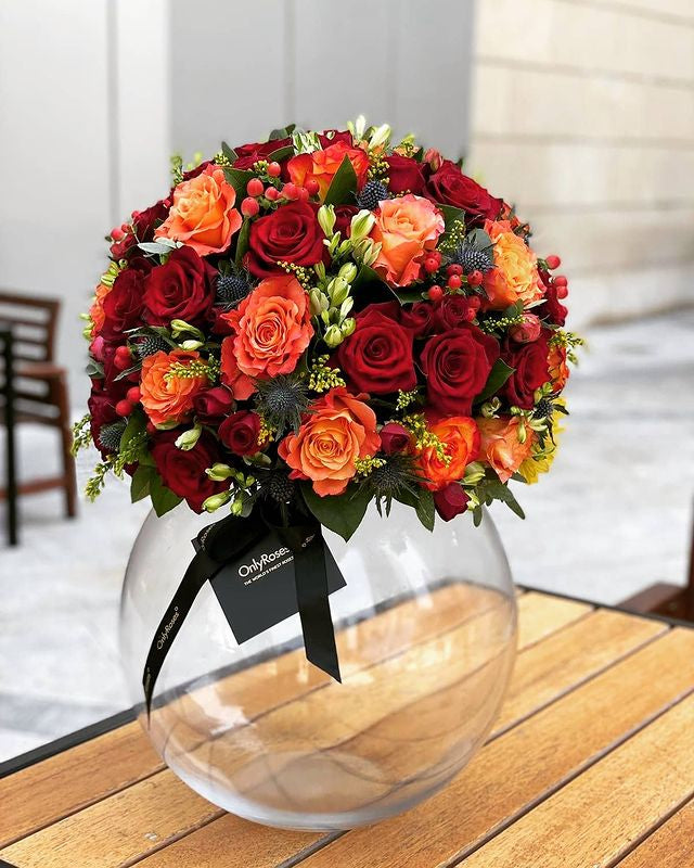 Bouquet of red and orange roses in a clear vase on a wooden surface.