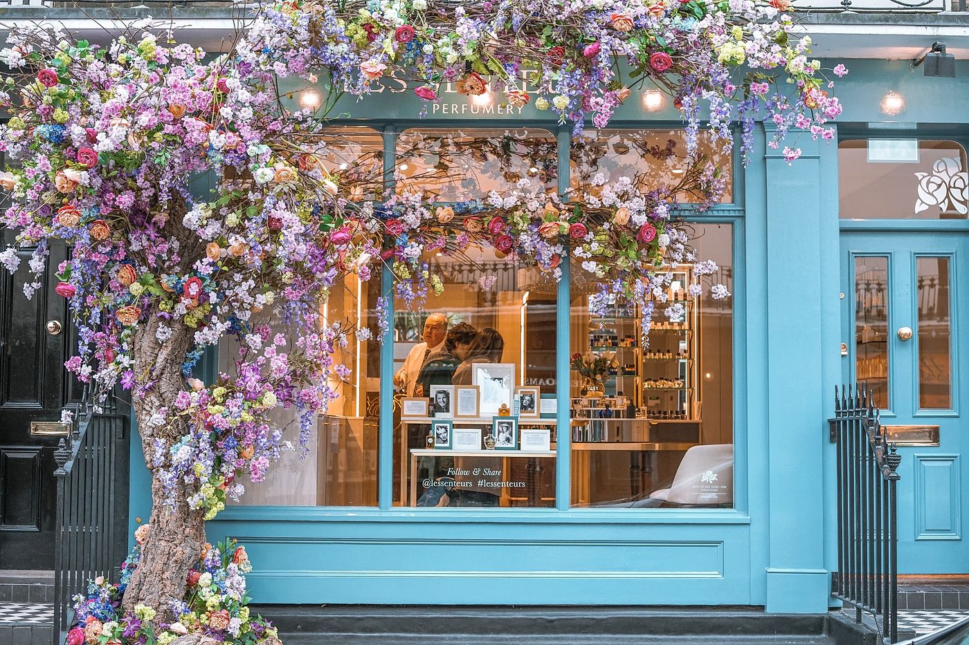 Blue storefront with floral decorations and a tree, featuring a display inside.
