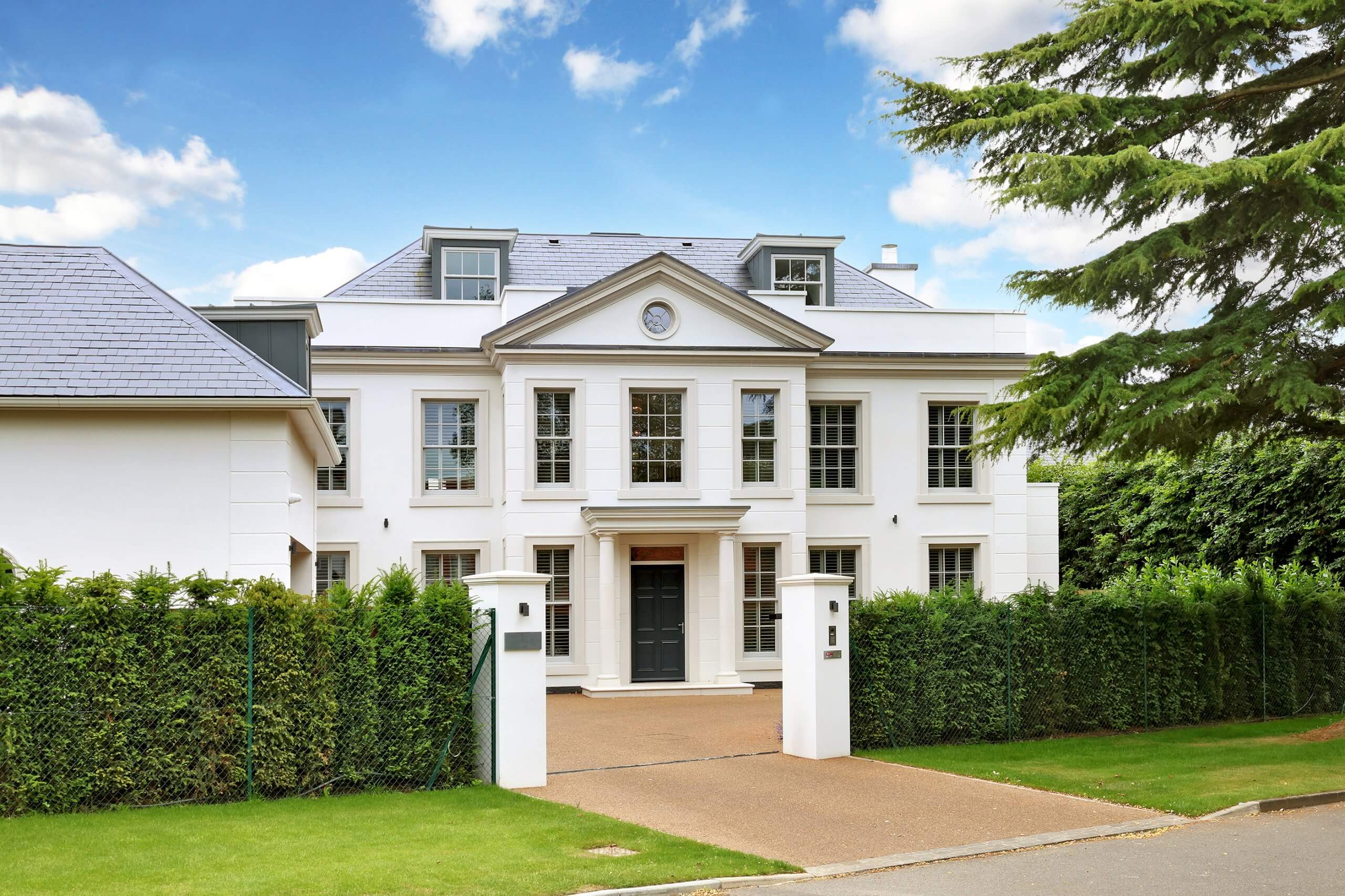 Large white house with a driveway and greenery under a blue sky