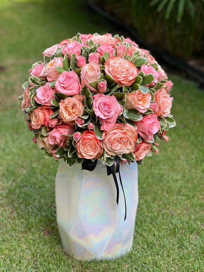 Bouquet of pink and peach roses in a iridescent vase on grass