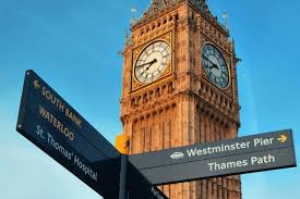 Big Ben clock tower with street signs pointing towards Waterloo, Westminster Pier, and Thames Path against a clear blue sky.